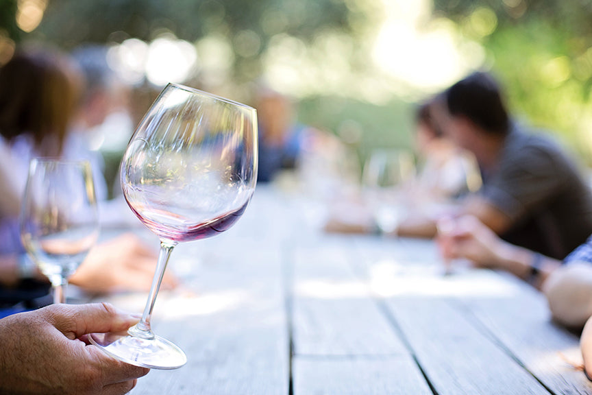 wine glass in forefront, people sitting at picnic table in blurred background